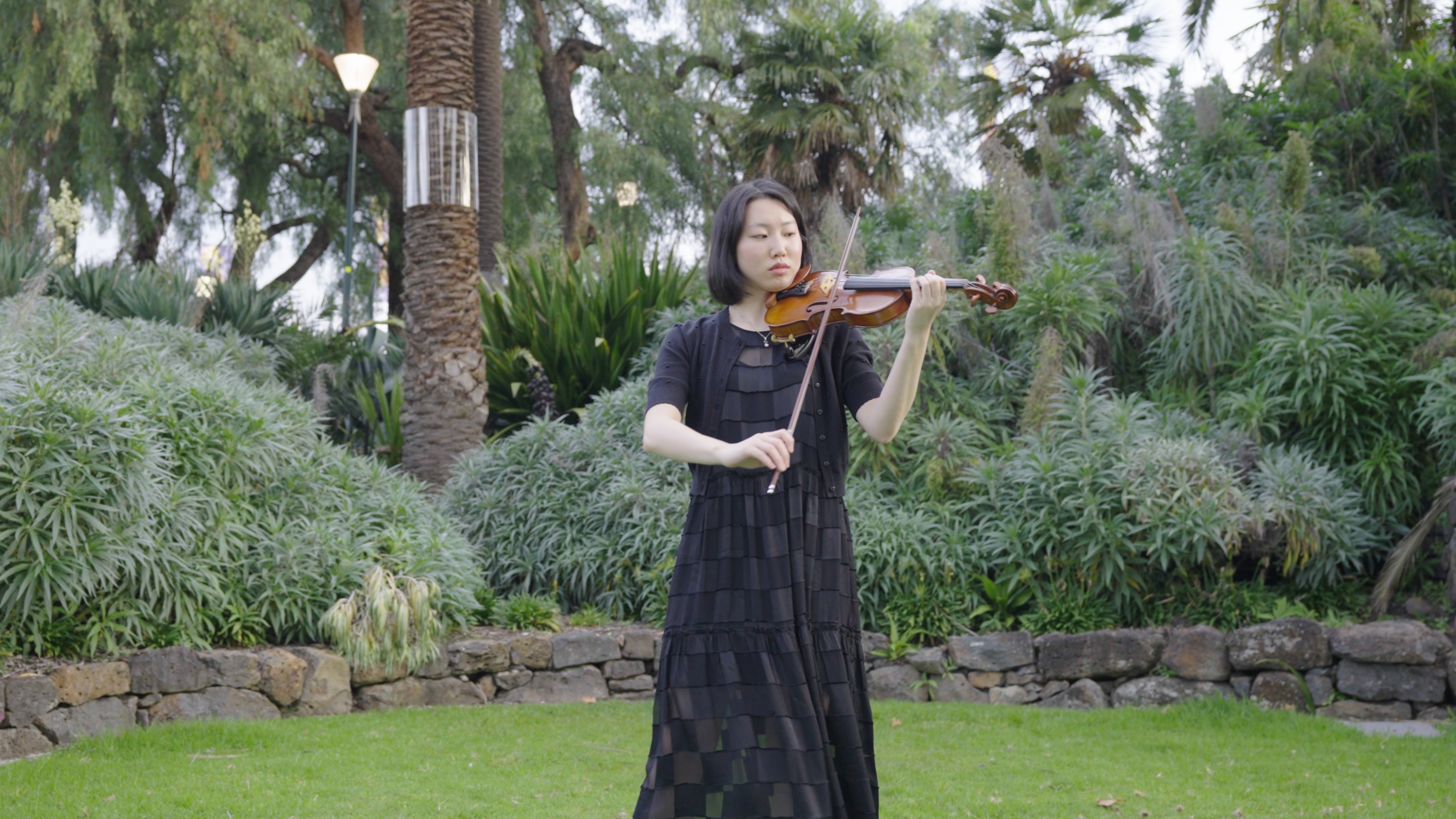 A woman playing a violin in a garden.